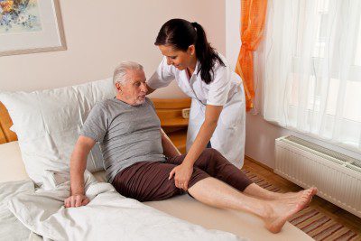 A care home nurse helping a resident get back into bed.