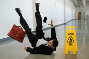 Man slips on wet floor and falls on back next to wet floor caution sign