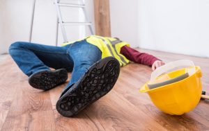 An unconscious worker lying on the ground with their hard hat discarded.