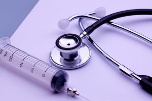 Syringe with needle and stethoscope on a table. 