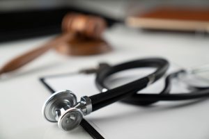 A stethoscope on a table with an out-of-focus gavel in the background. 