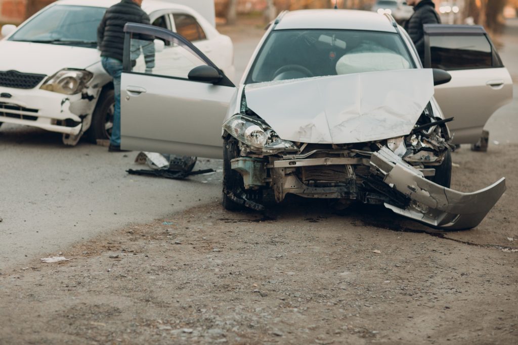 The front of a grey car smashed on the road with the doors open. 