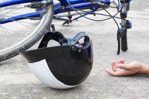 An injured person laying on the ground next to their helmet and crashed bicycle