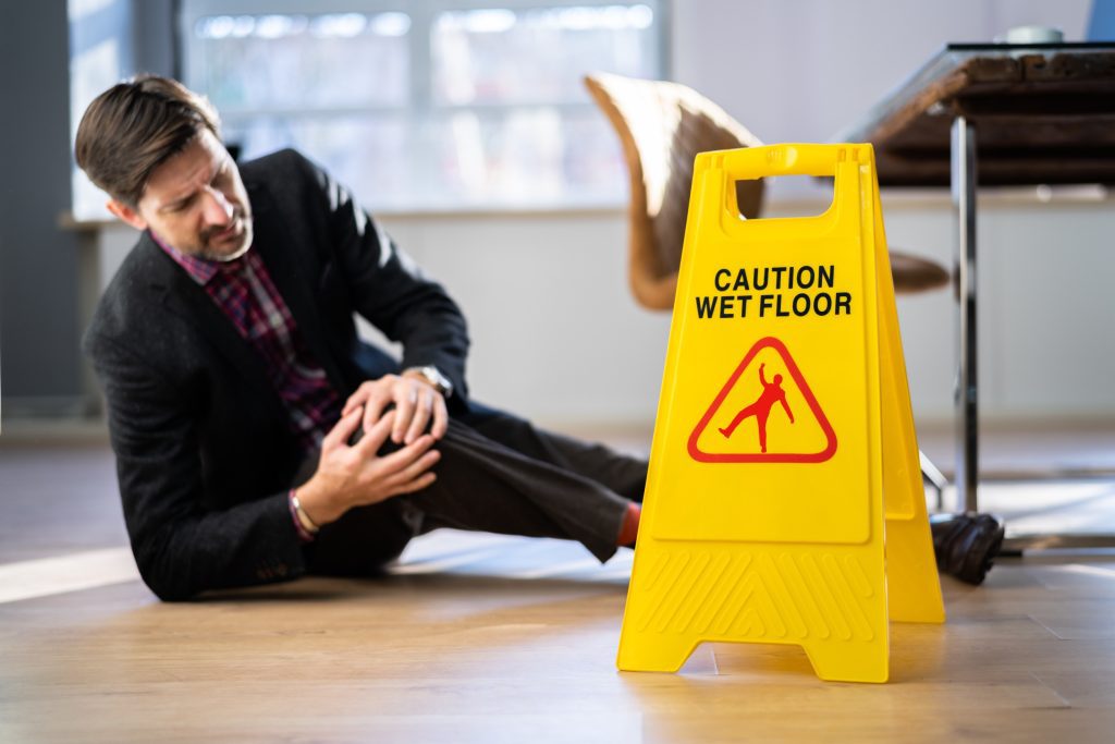 A man holding his knee in pain next to a wet floor sign.