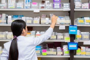 A pharmacist reaches for a packet of medicine on a pharmacy shelf.