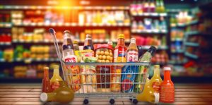 A trolley with different food items and a blurred out background of supermarket shelves.