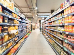 A blurred image of a supermarket aisle with food shelves either sides.