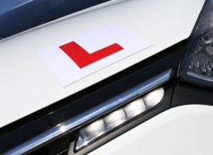 A close up shot of a car with a L plate attached to the bonnet