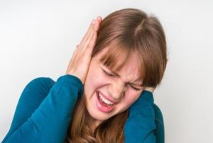 A woman in discomfort covering both of her ears with her hands