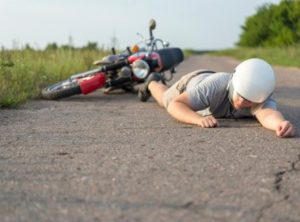 Injured rider wearing a helmet lying on the road in front of crashed motorbike