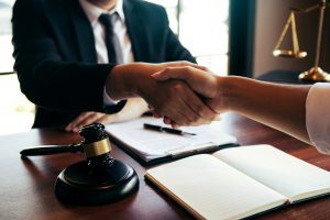 A solicitor shakes hands with a client over a desk after explaining NHS data breach compensation. 