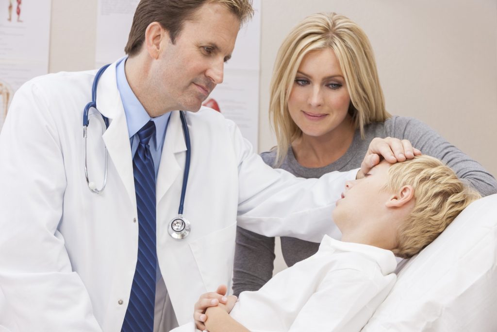 A doctor standing above a patient who is lying in bed and placing a hand on their head.