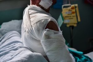 A person sits on a bed, wrapped in bandages. 