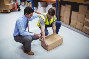 A man in a suit shows a warehouse worker the correct way to lift a box