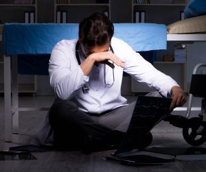 A doctor sat on the floor of their office with a hand covering their face.