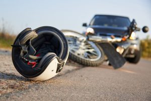 A motorcycle helmet is in the foreground, behind is a crashed bike and a car. 