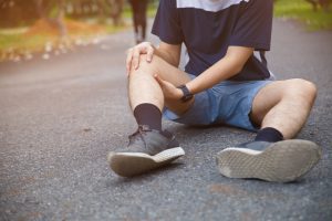 A man sits on the path in a park, holding his leg. 