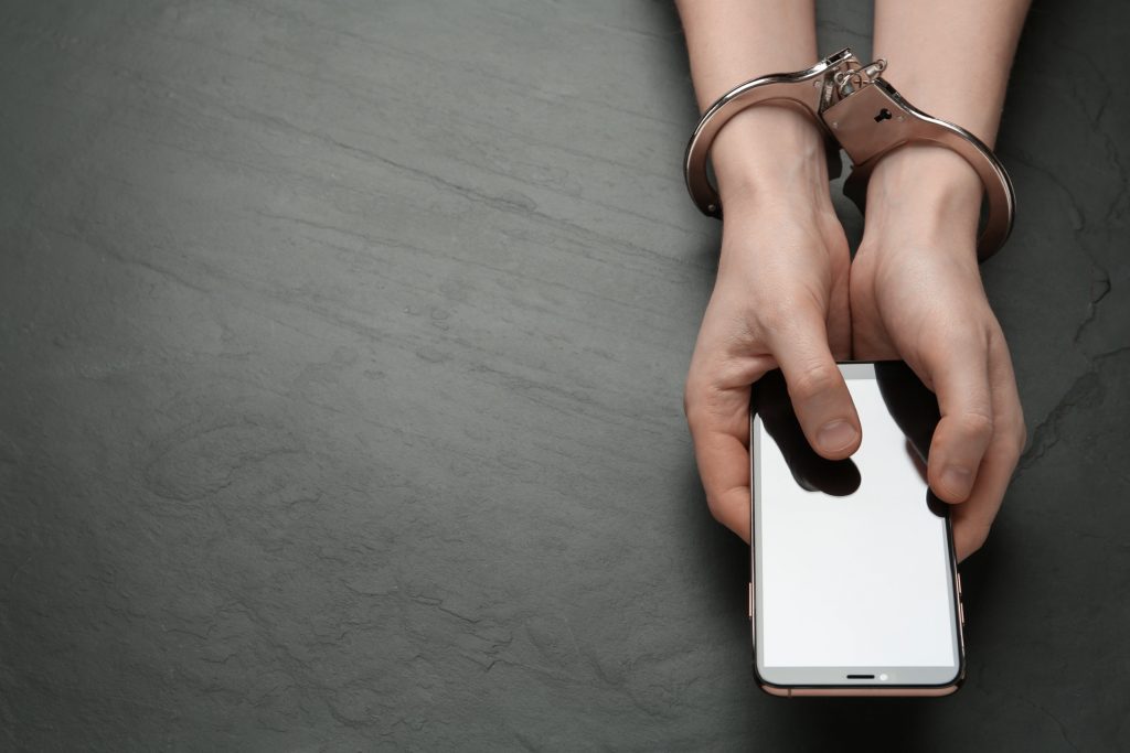 Person with handcuffs on holding mobile phone 