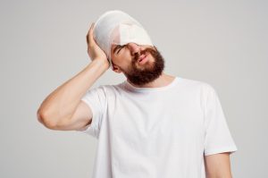 A man with a bandage wrapped around his head holding it in pain.
