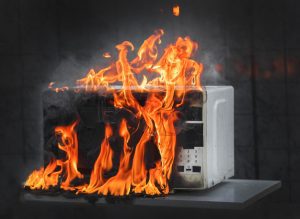 A microwave that is on fire, with flames surrounding it.