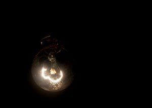 A dimly lit light bulb hanging upside down in a pitch-black room, signifying poor lighting in the workplace.