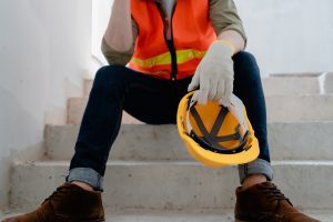 A worker sits on the stairs holding a hard hat.