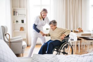 IMAGE OF ELDERLY PERSON IN A CARE HOME BEING HELPED OUT OF A WHEELCHAIR