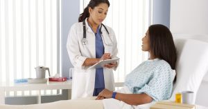 A doctor standing and talking to a patient who is lying in a bed.