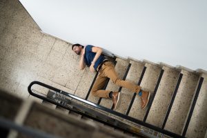 A man lays at the bottom of a staircase having fallen down them. 