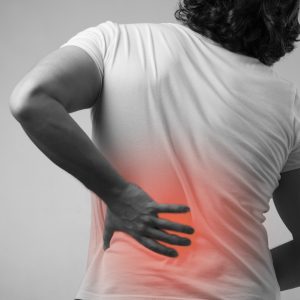 A person in a white t-shirt places their hand on their painful lower back.