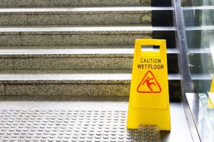 A yellow plastic sign warns of a wet floor at the bottom of a concrete staircase.