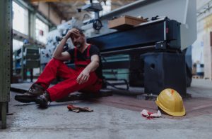 INJURED FACTORY WORKER SEATED BY FAULTY EQUIPMERNTY AFTER CUTTING HAND