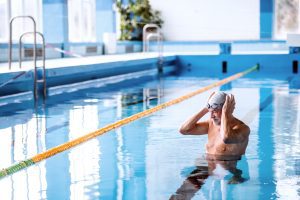 A man adjusts his swim cap and goggles in a pool. 