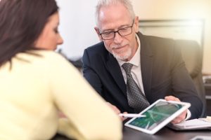 A solicitor wearing glasses and a black suit explains to a woman wearing a yellow top how she can claim on a No Win No Fee basis.