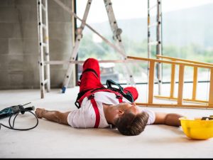 A worker lays on the floor by a ladder. 