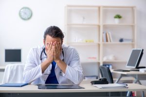 DOCTOR WITH HEAD IN HANDS AT DESK 