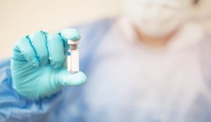 A doctor wearing gloves holds an anaesthetic vial. 