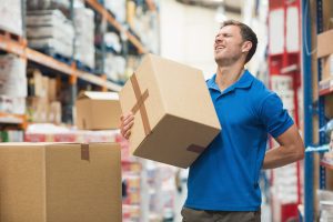 A worker lifts a box, holding their back in pain.