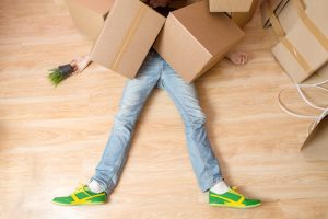 A worker lays on the floor under boxes.