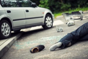 A man lying on the ground after being hit by a white car that is driving on the pavement 