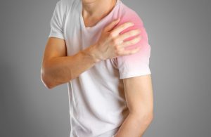 A man in a white t-shirt holding his shoulder in pain.