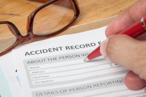 Person uses red pen to fill out form entitled 'accident record' on a table