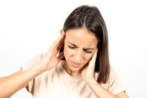 woman clutching head because of hearing damage in one or both ears