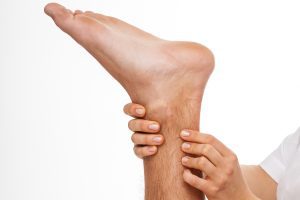 Physiotherapist holds person's foot aloft while massaging their Achilles tendon.