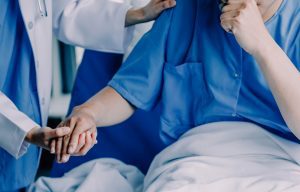 Doctor holds patient's hand as they sit up in hospital bed to cough.