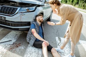 A man with a knee injury after being involved in a car accident sat leaning against a car on a zebra crossing. 